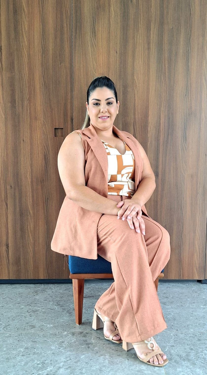 Gabriela Reis, arquiteta e sócia da Magare, sentada diante de um painel de madeira