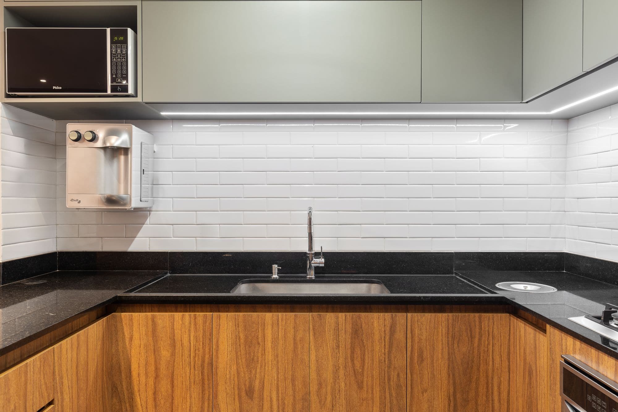 Cozinha com armários amadeirados, aéreos verde-claros e revestimento branco