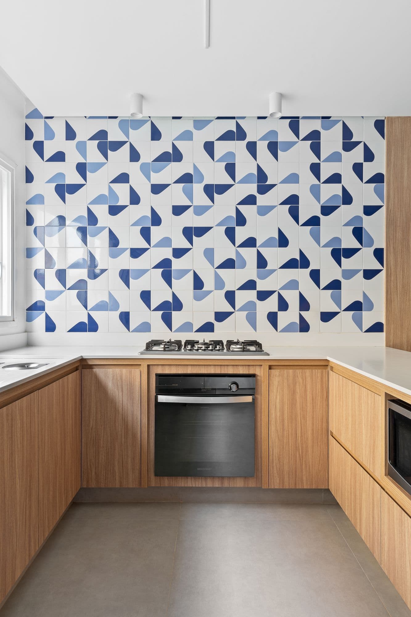 Cozinha em U com marcenaria amadeirada e revestimento geométrico azul e branco