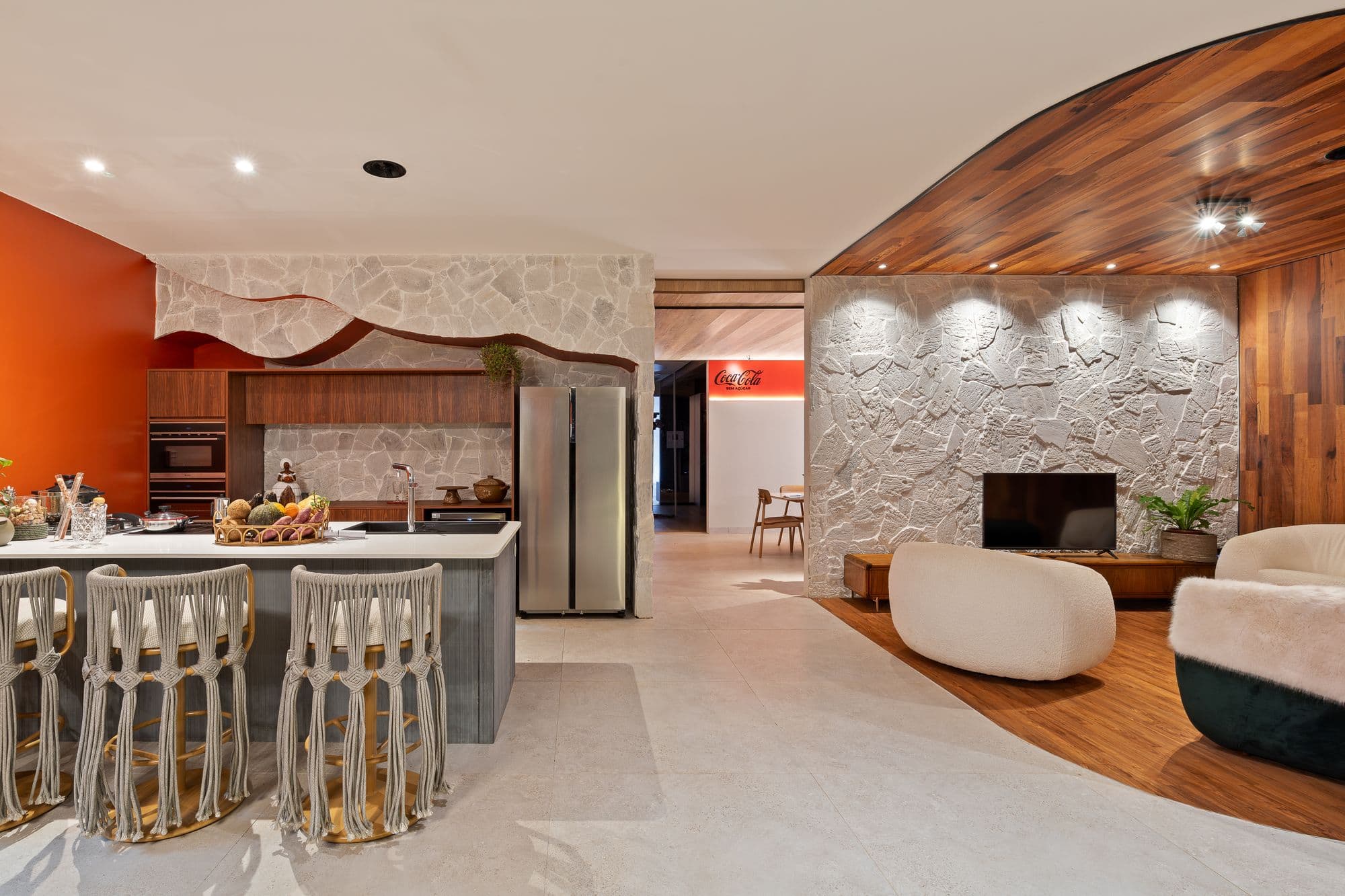 Sala de estar integrada à cozinha, com forro de madeira curvo, na CASACOR 2024